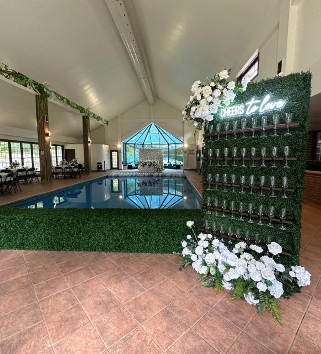 Wedding champagne wall set up with a cheers to love neon with white roses and greenery