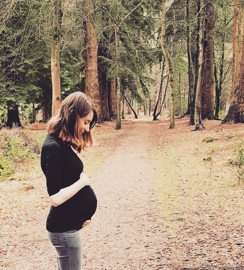 pregnant woman standing in a forest holding her bump