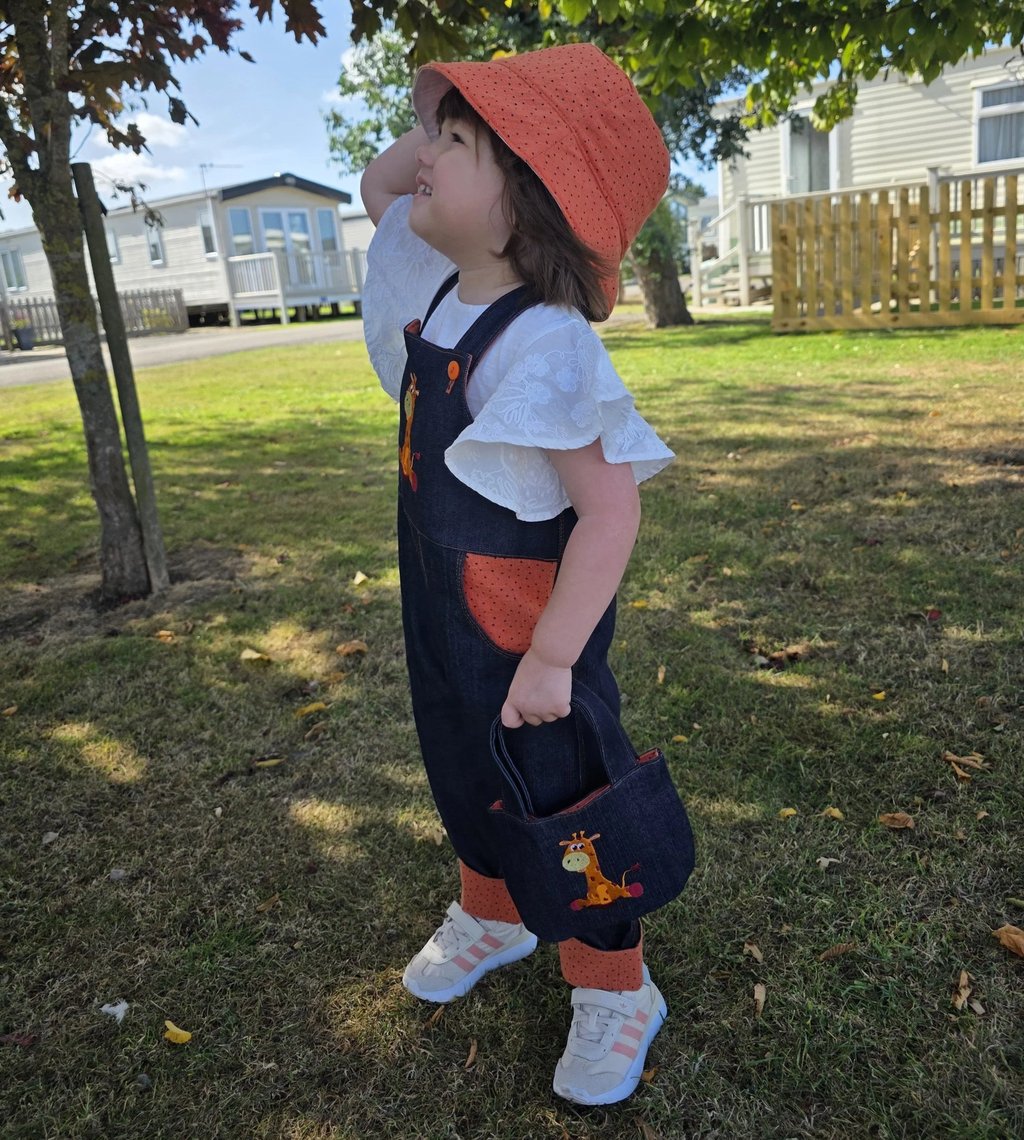 Toddler in denim giraffe dungarees and orange sun hat, made in Nottingham UK
