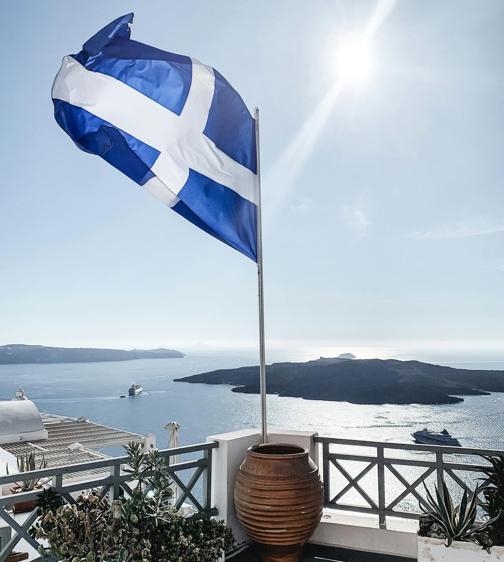 a Greece flag on a balcony with a potted planter