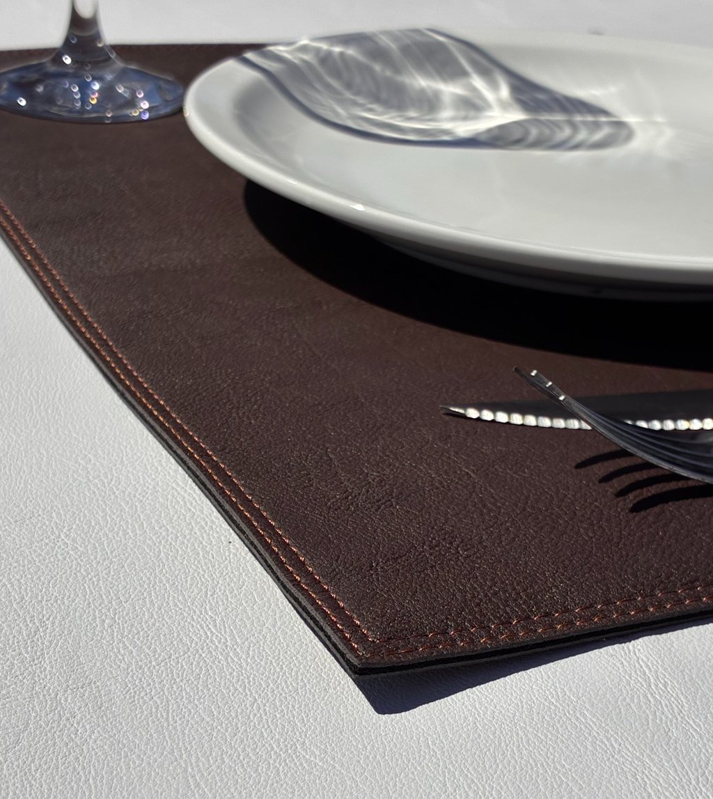 Foto detalle de una esquina de un individual de similcuero, ambientado con plato, copa y cubiertos