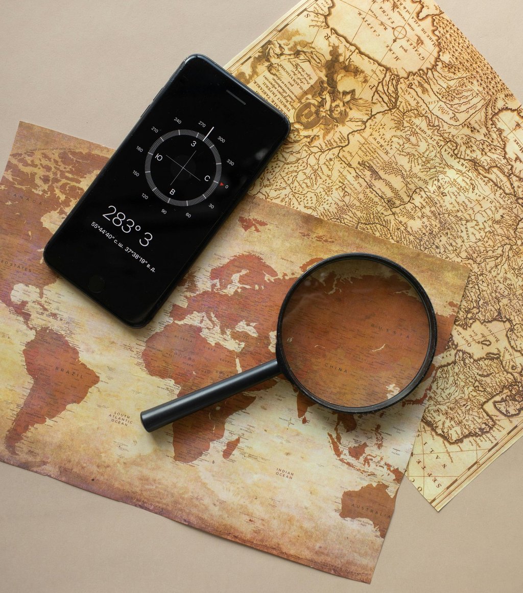 Smartphone and magnifying glass over survival maps, showing digital and analog navigation