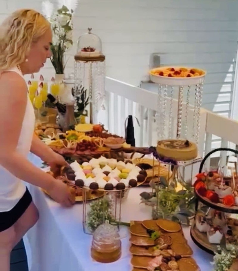 Una mujer organiza un buffet de brunch gourmet con postres, pasteles y aperitivos en un balcón.