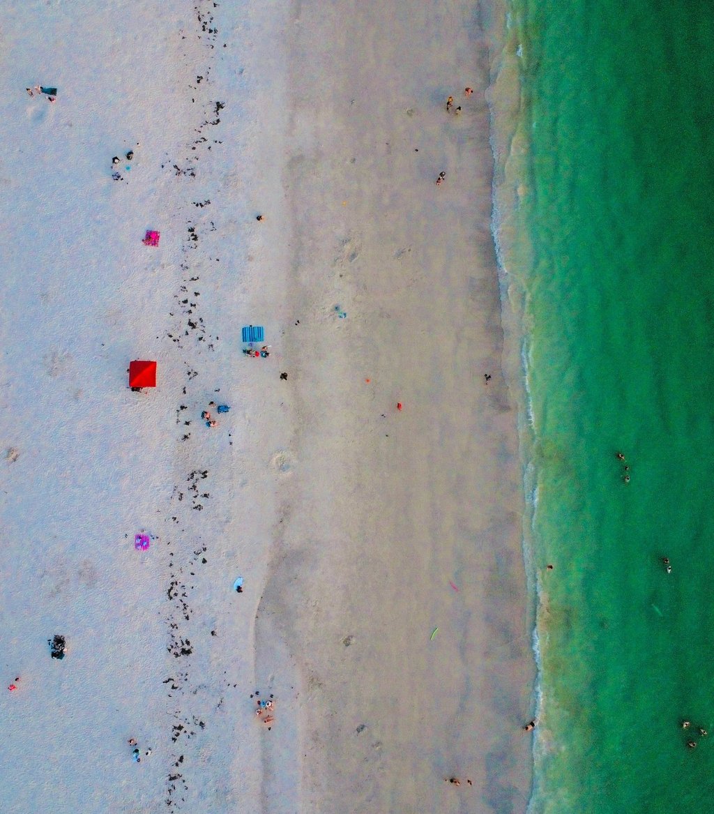 Aerial view of a white sand beach with turquoise ocean water and colorful umbrellas.