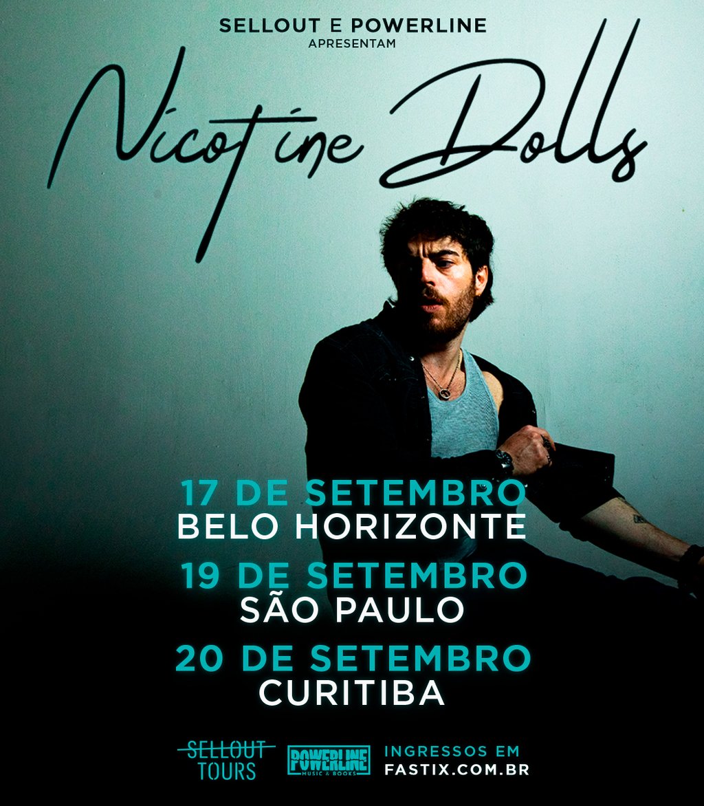 Plano médio de Sam Cieri, vocalista do Nicotine Dolls, sentado e posando contra uma parede azul