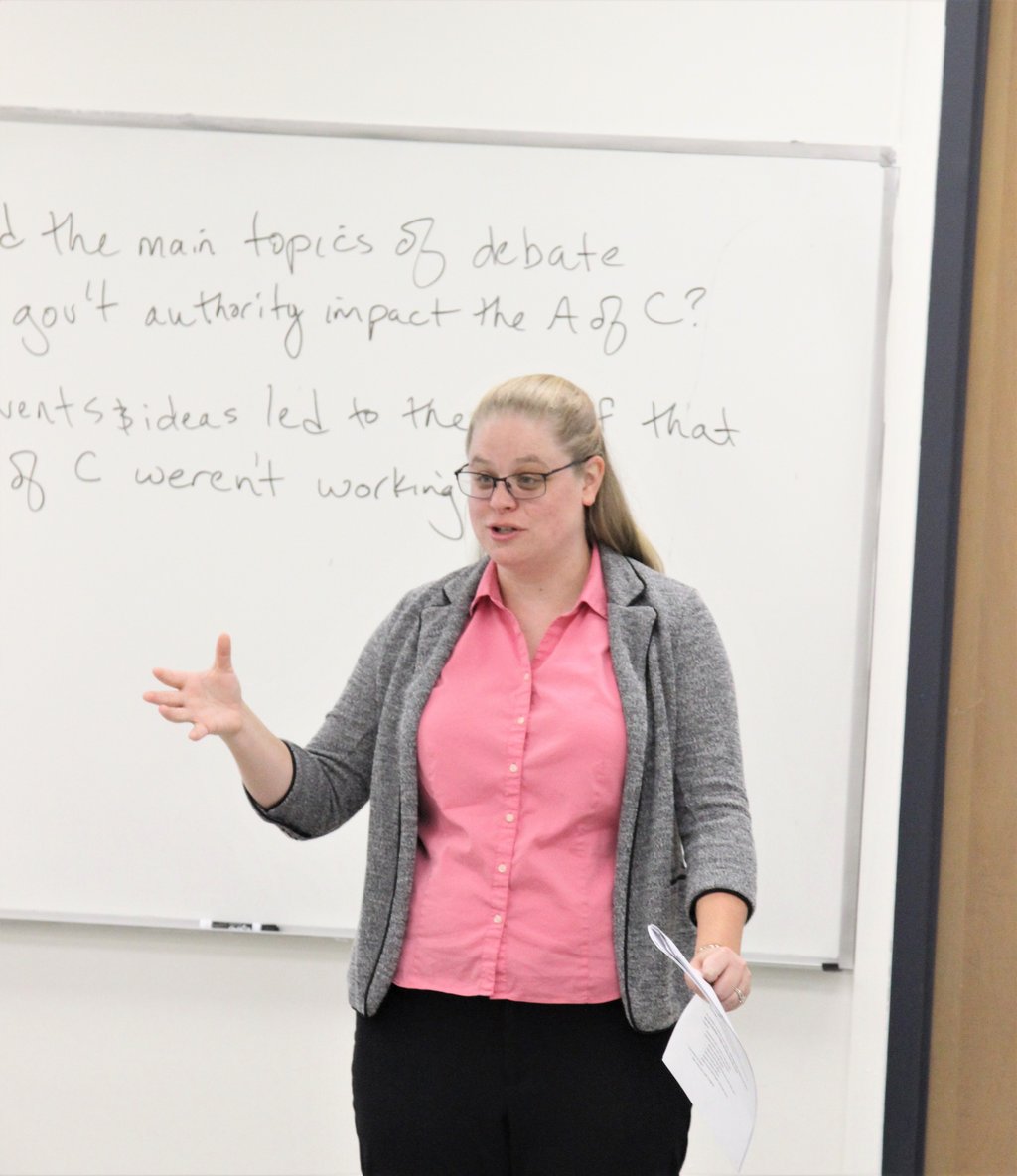 Dr. Hooton in front of a white board at the front of a classroom, teaching.