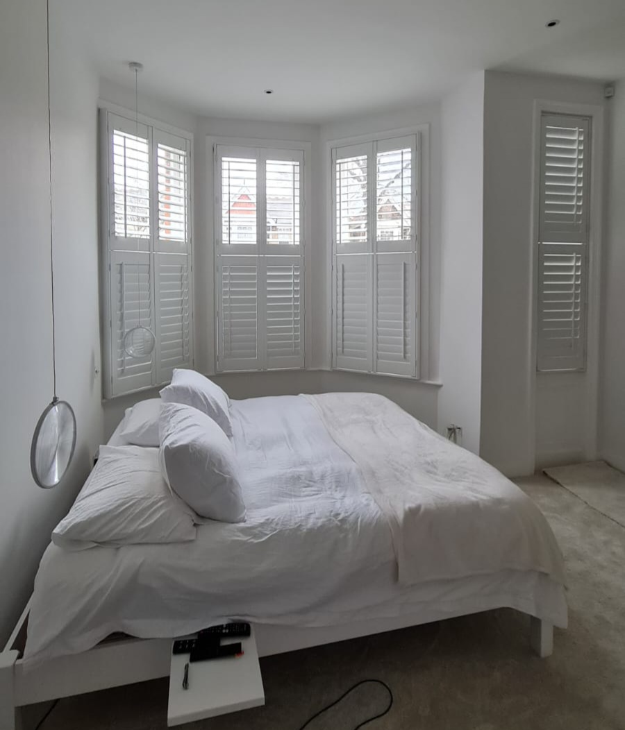Beautifully restored plantation wood shutters on a bay window in a bright Twickenham bedroom