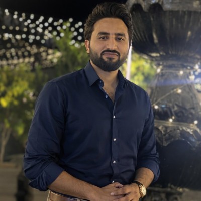 A bearded man in a navy blue button-down shirt posing outdoors at night with decorative lighting.