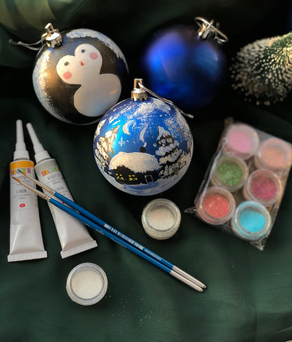 Hand-painted blue Christmas ornaments with brushes, glitter, and craft paint for DIY holiday decorating.