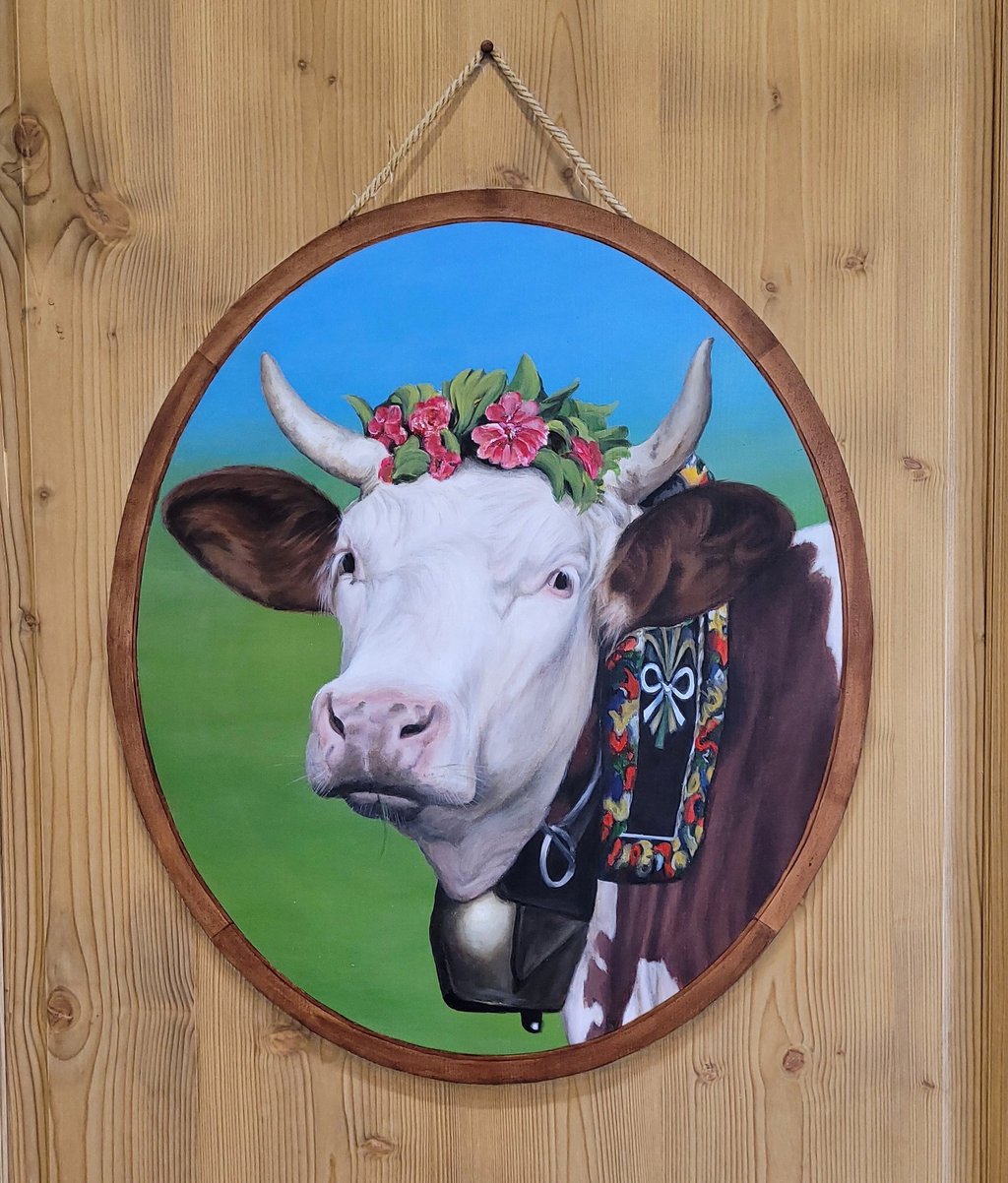Une tête de vache Montbéliarde ornée de fleurs peinte en trompe-l'oeil dans son faux médaillon