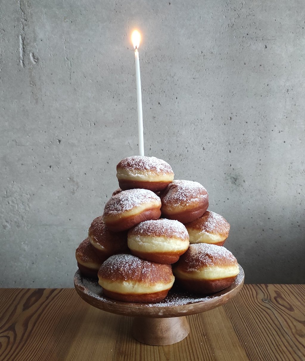 Pączki ułożone w stos na paterze z wbitą urodzinową świeczką na czubku