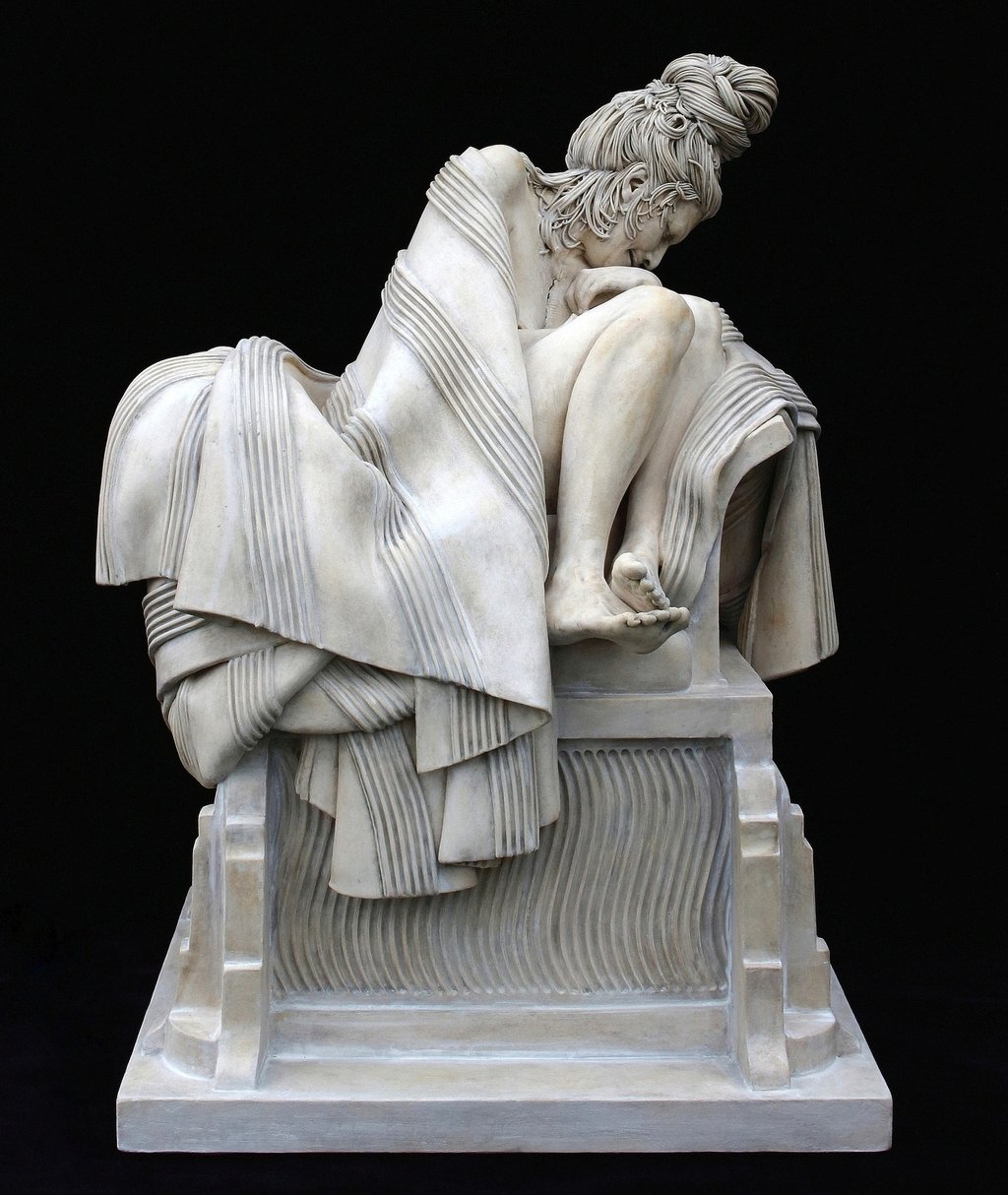 Ceramic sculpture of grieving woman wrapped in blanket on large classical plinth.