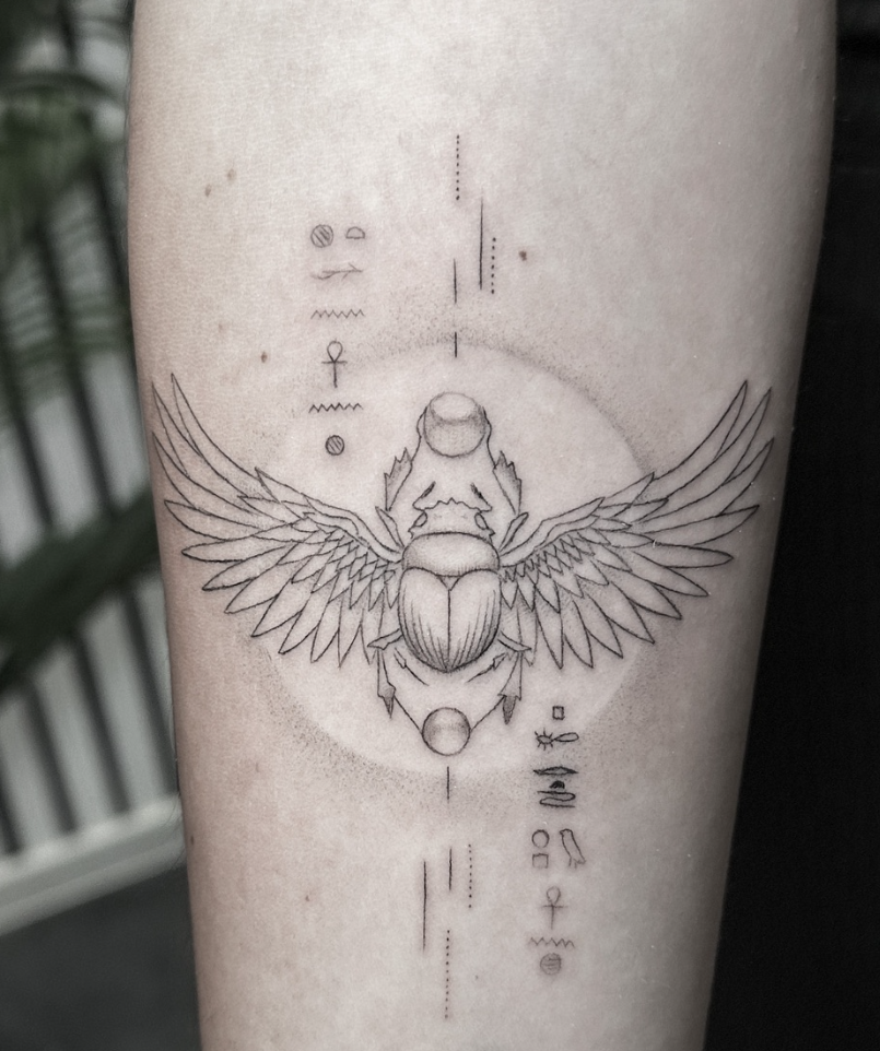 Tatuaje fineline escarabajo egipcio alado con jeroglíficos en antebrazo madrid