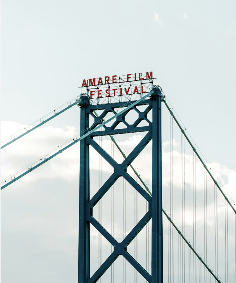 Red Amare Film Festival sign atop a blue steel suspension bridge tower against a cloudy sky.