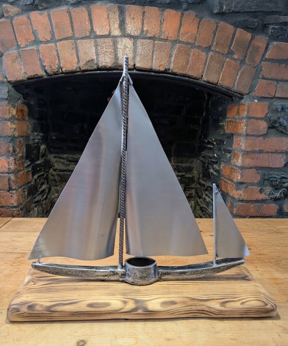 A large sailboat sculpture made from recycled metal materials sitting on a scorched wood stand