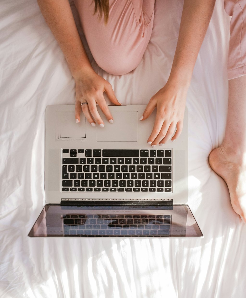 a woman sitting on a bed with her laptop computer