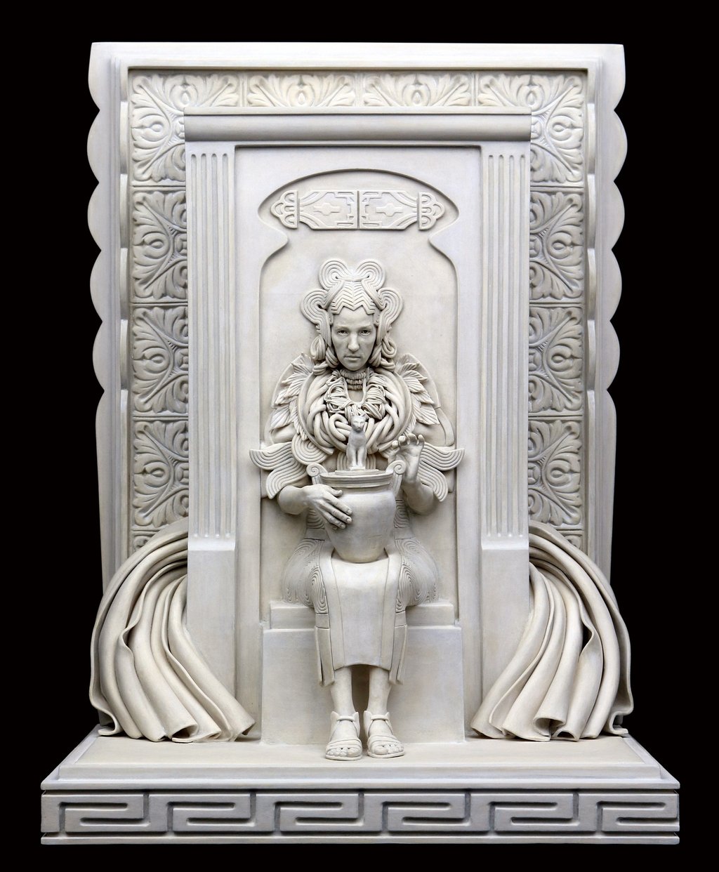 Ceramic sculpture of woman embedded in wall, wearing heavy jewelry and elaborate dress, holding Egyptian cat urn.