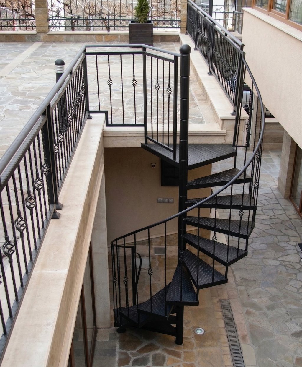 Black outdoor metal spiral staircase with decorative wrought iron railings leading to a stone patio.