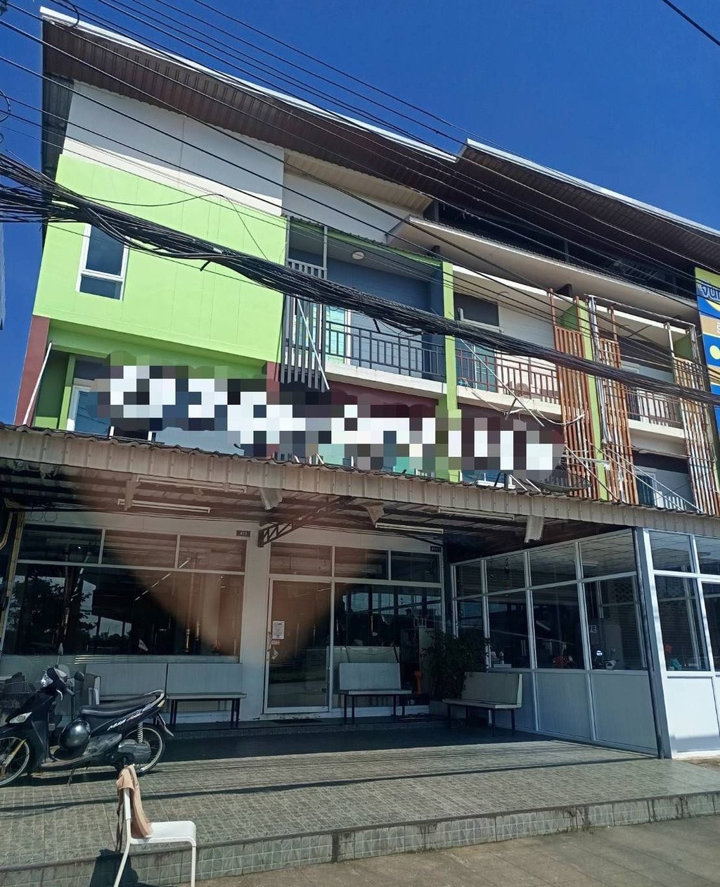 A modern three-story green and white office building with large glass windows and parked motorbikes out front.