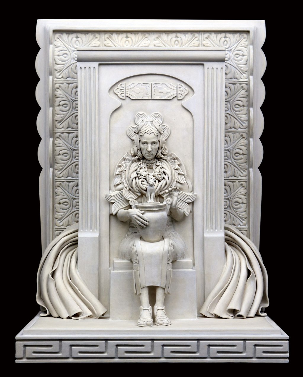 Ceramic sculpture of woman embedded in wall, wearing heavy jewelry and elaborate dress, holding Egyptian cat urn.