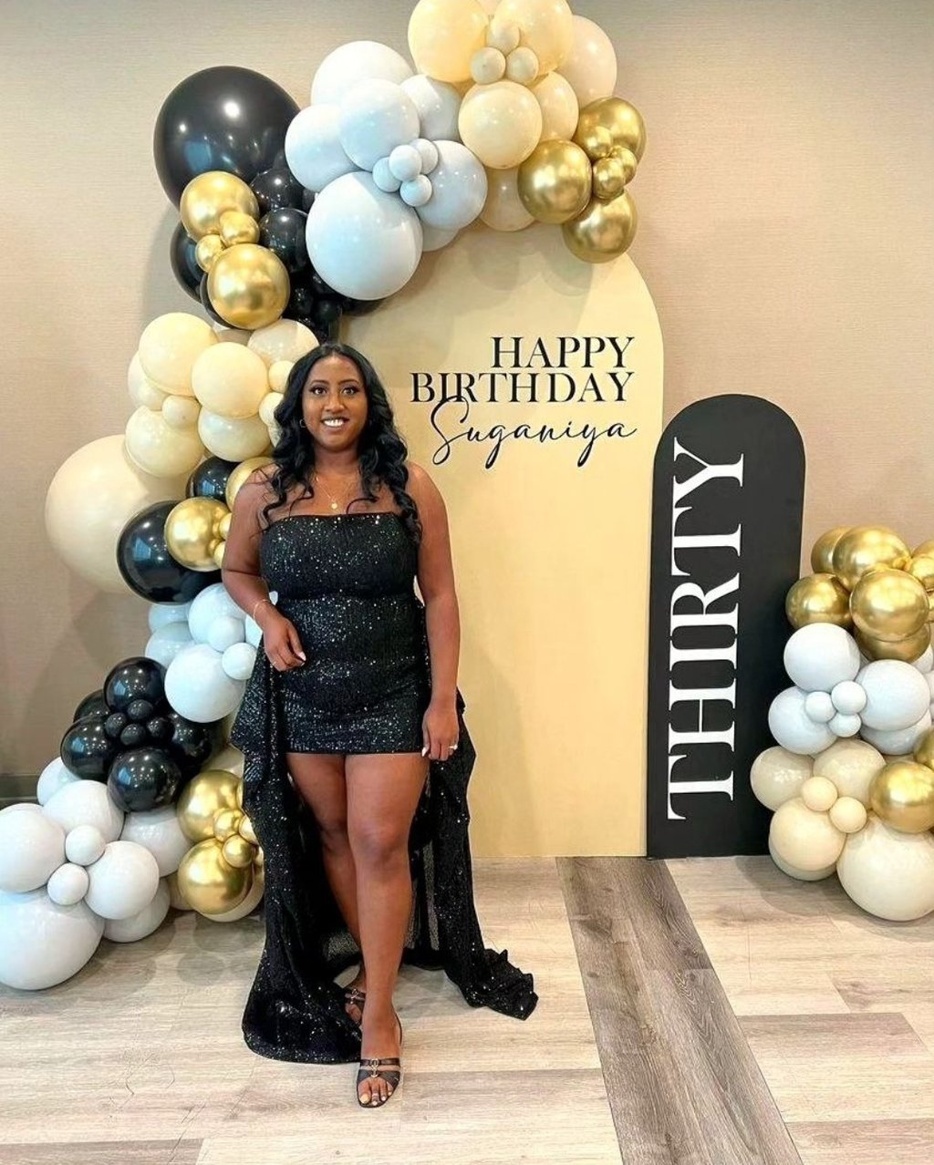 a woman in a black dress standing in front of a birthday sign
