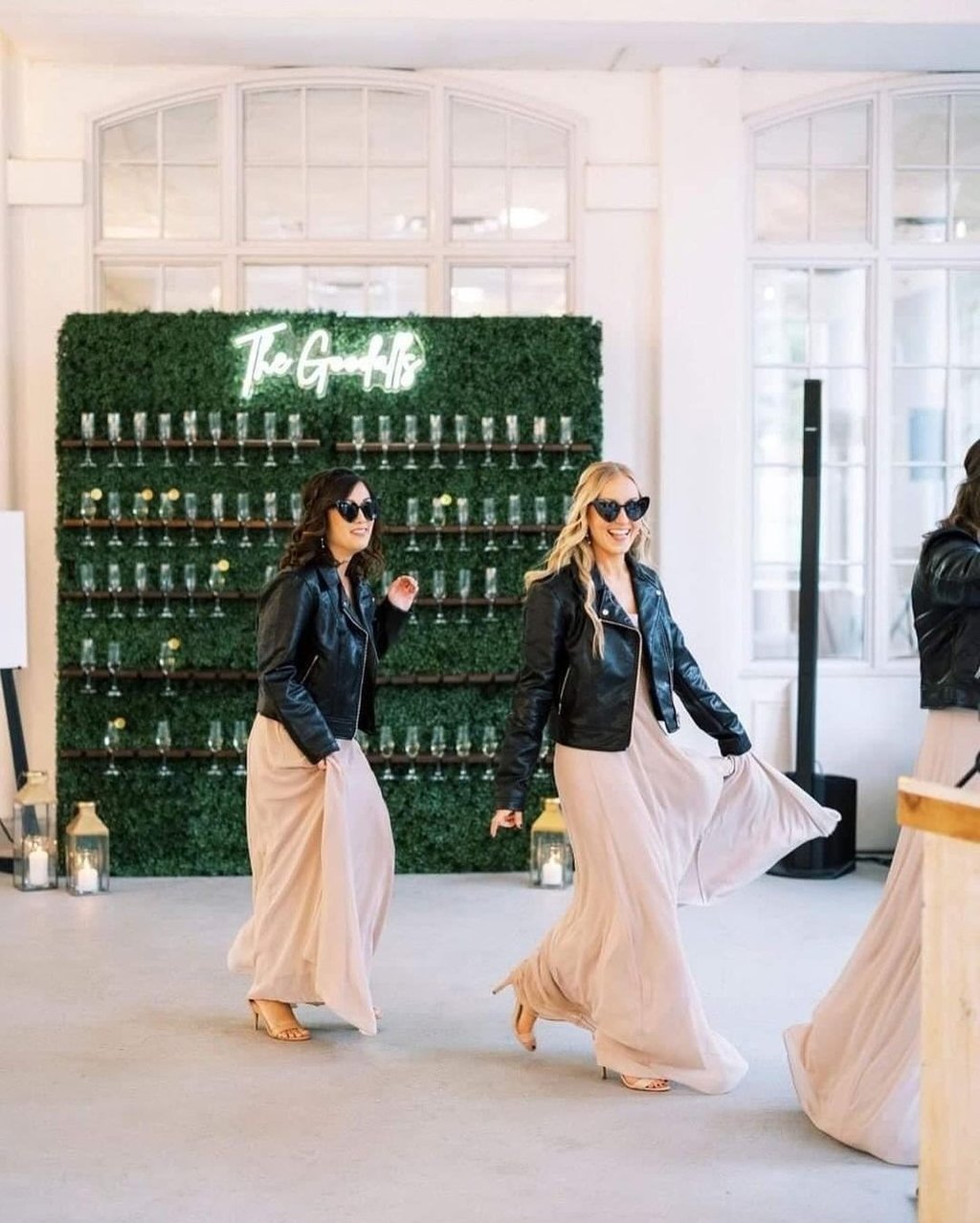 Bridesmaids walking past the grass champagne walls behind them.