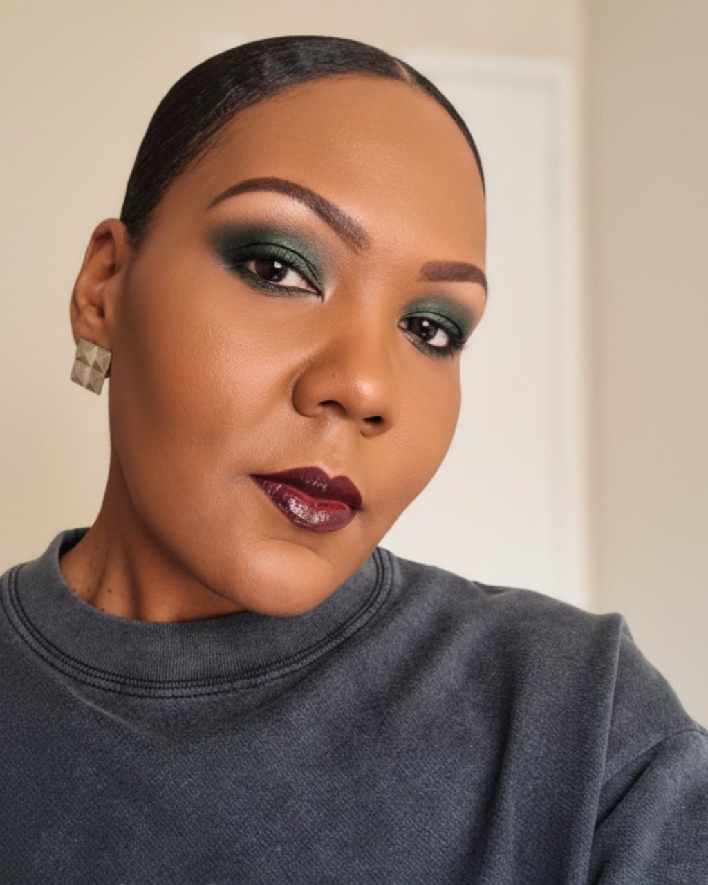 A woman with flawless makeup featuring emerald green eyeshadow and a deep plum glossy lip.