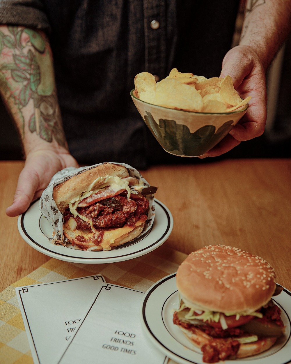 Dan holding a Winnipeg Fat Boy style burger and chips over a table.