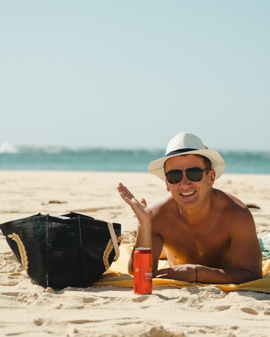 pessoa relaxando na praia em dia ensolarado com bolsa de praia e bebida refrescante