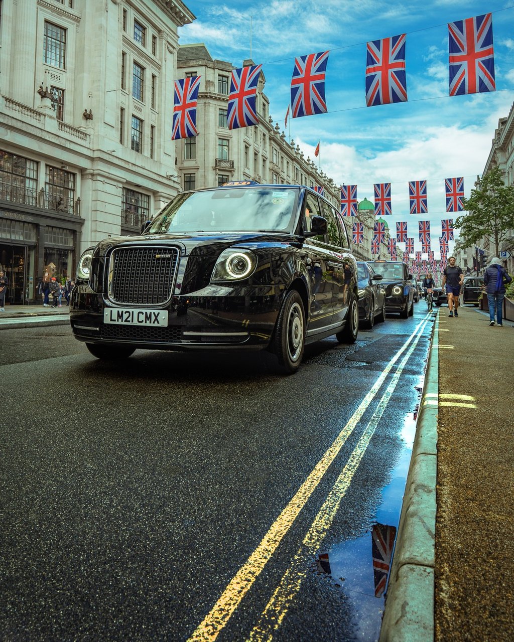 táxi preto tradicional circulando por rua de Londres com bandeiras britânicas