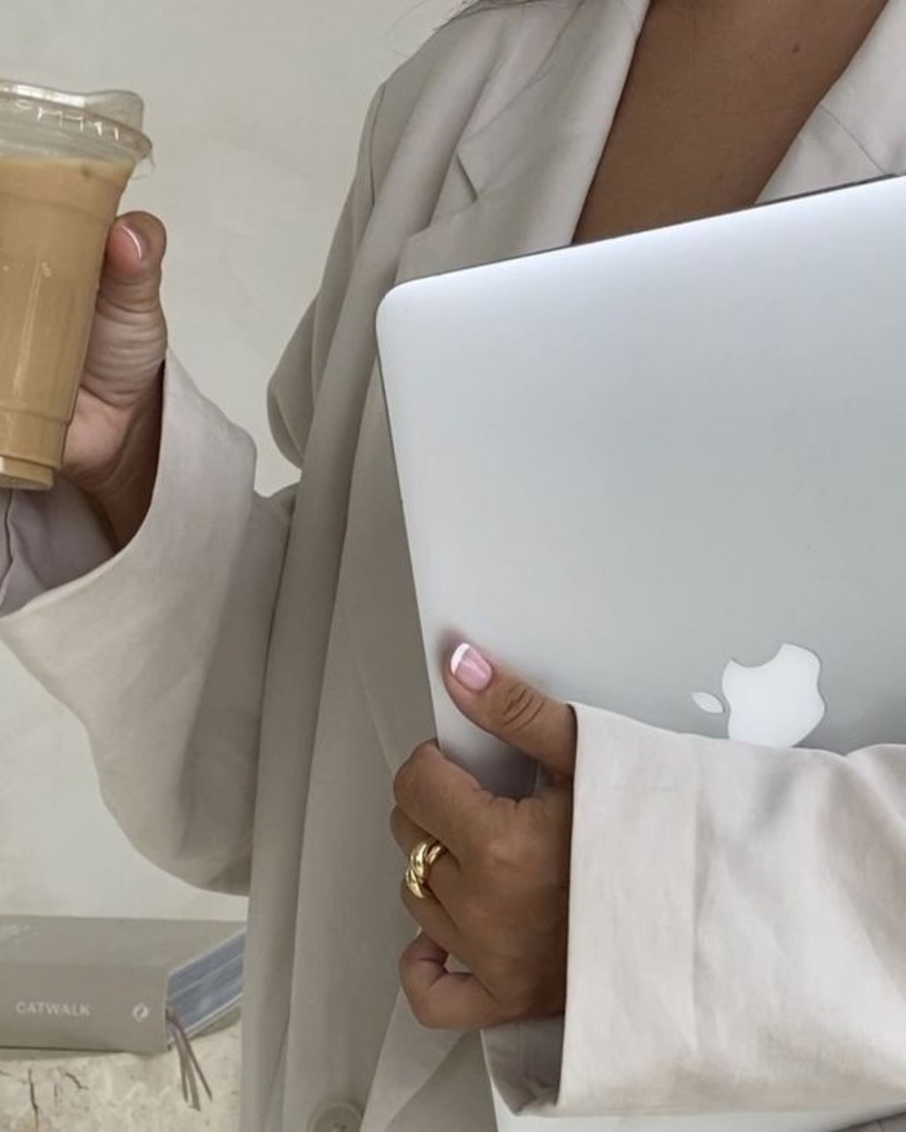 Ženska osoba, poslovna, u ruci drži Macbook, u drugoj ledenu kavu.