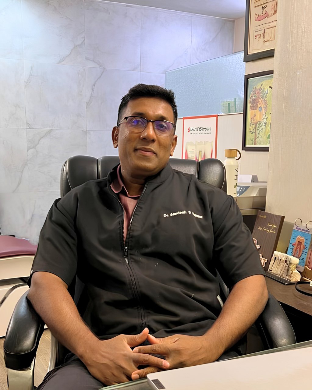Dr. Sandesh Kumar, an experienced implant dentist, sitting in his dental clinic office.