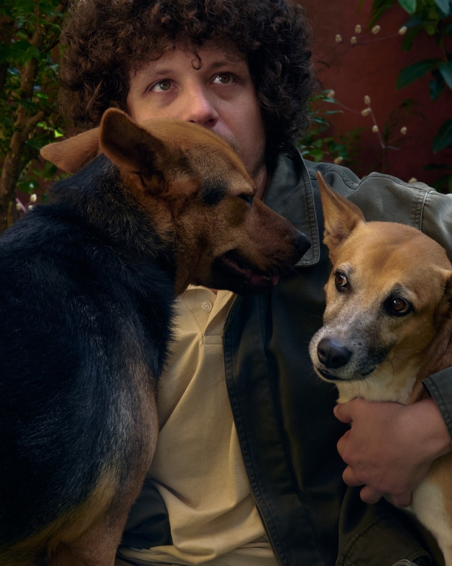 Foto do cantor Chico Chico com dois cachorros em um local aberto. 