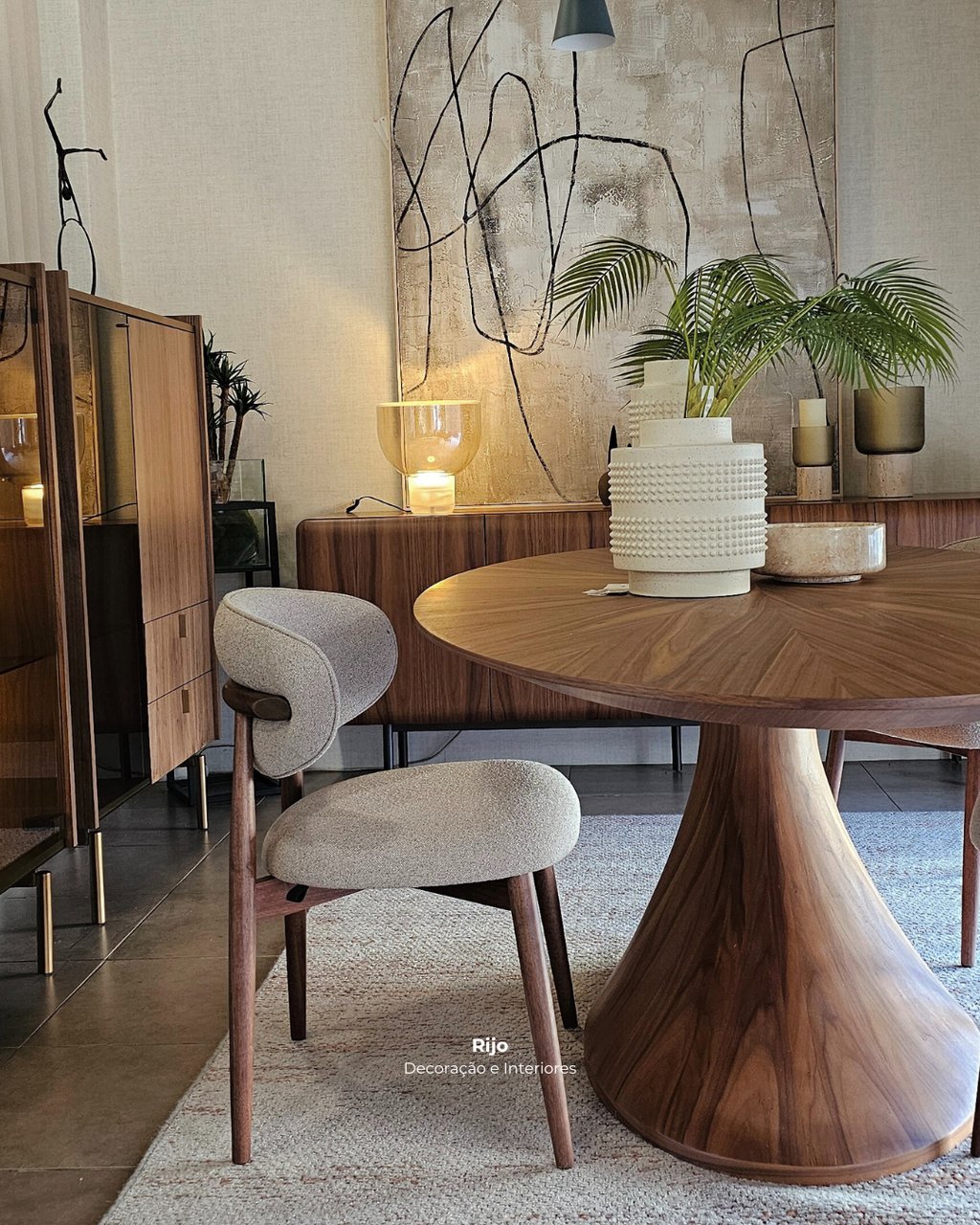 Modern dining room featuring a round walnut table and stylish grey upholstered chair with abstract wall art.