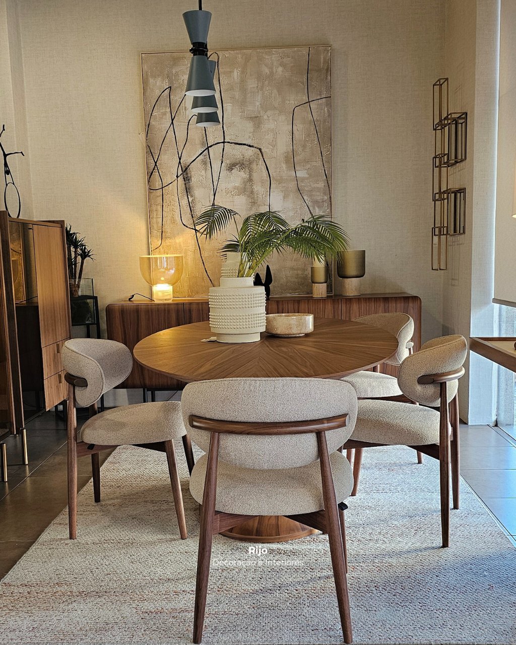 Modern dining room featuring a round walnut table and four beige upholstered chairs on a textured rug.