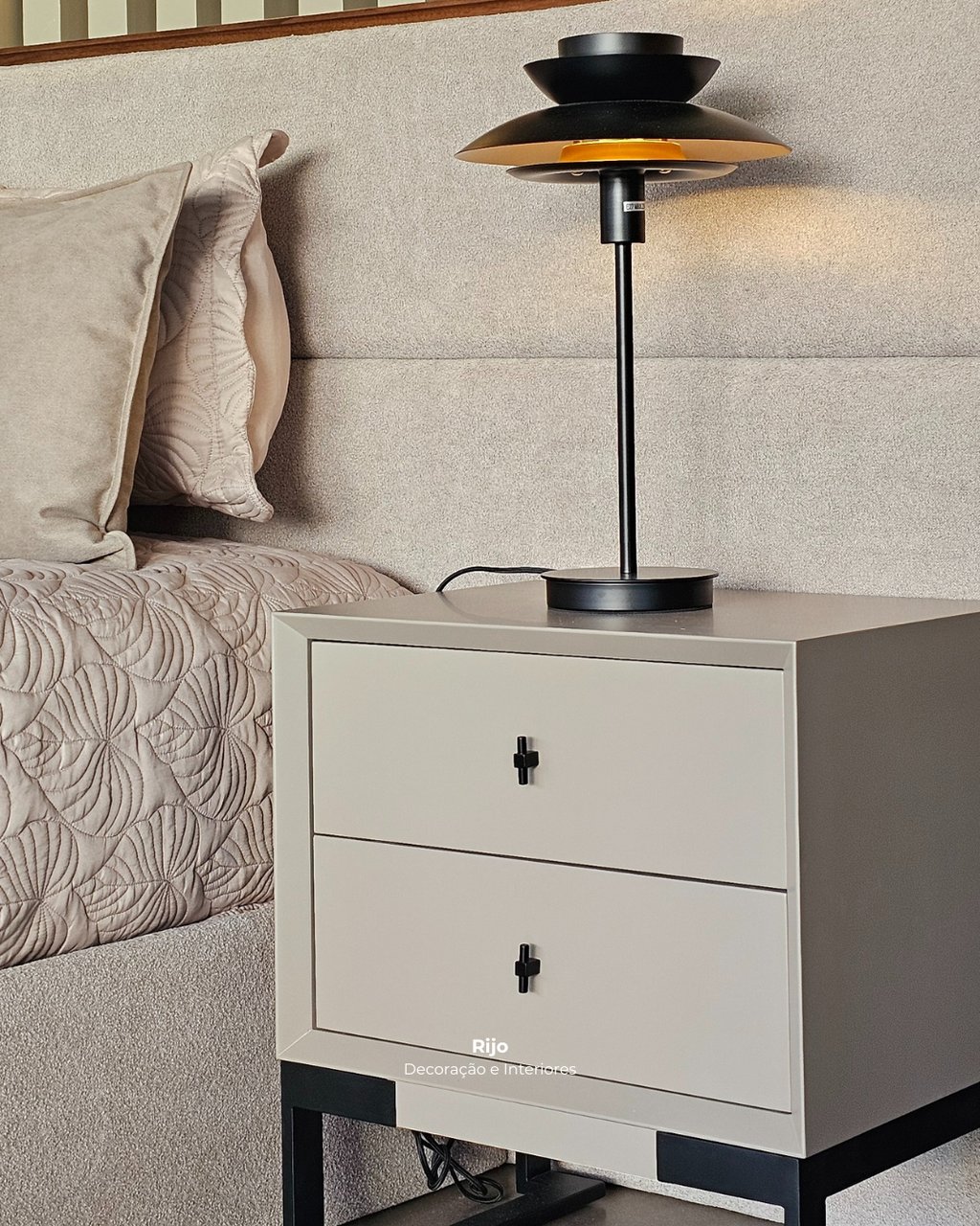 Modern beige nightstand with black handles and a sleek black metal lamp in a cozy bedroom setting.