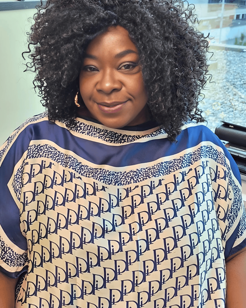 Smiling woman with voluminous curly hair wearing a blue and white patterned designer tunic top.