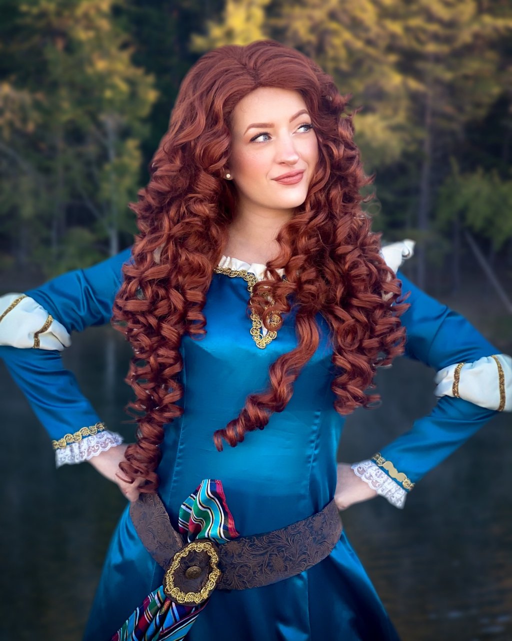A woman in a Merida cosplay featuring long curly red hair and a teal medieval gown outdoors.