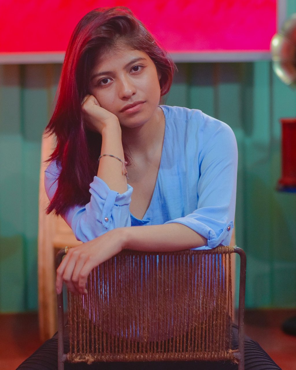 A young woman with auburn hair in a blue blouse sits on a vintage chair.