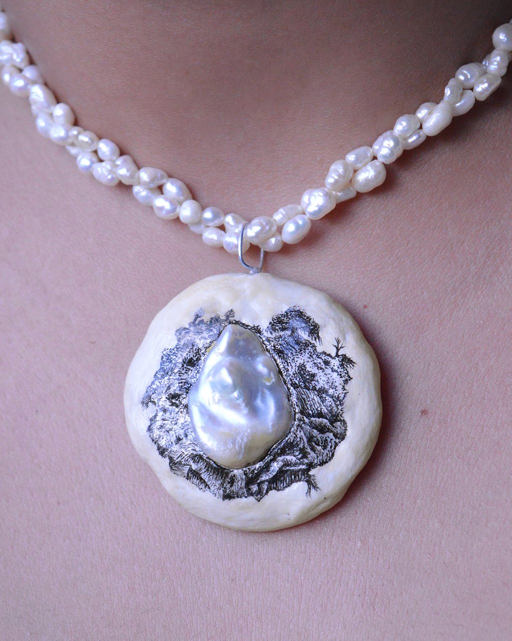 A string of pearls with a pendant made of clay. Pendant includes a  hand-drawn landscape in ink.