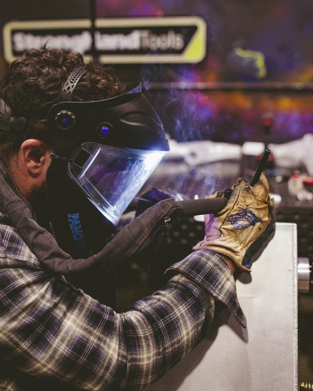 Professional welder wearing a protective mask and gloves while welding metal at Stronghand Tools.