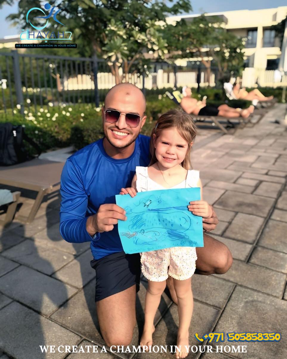 Smiling private swim coach and young student holding a drawing by a swimming pool.