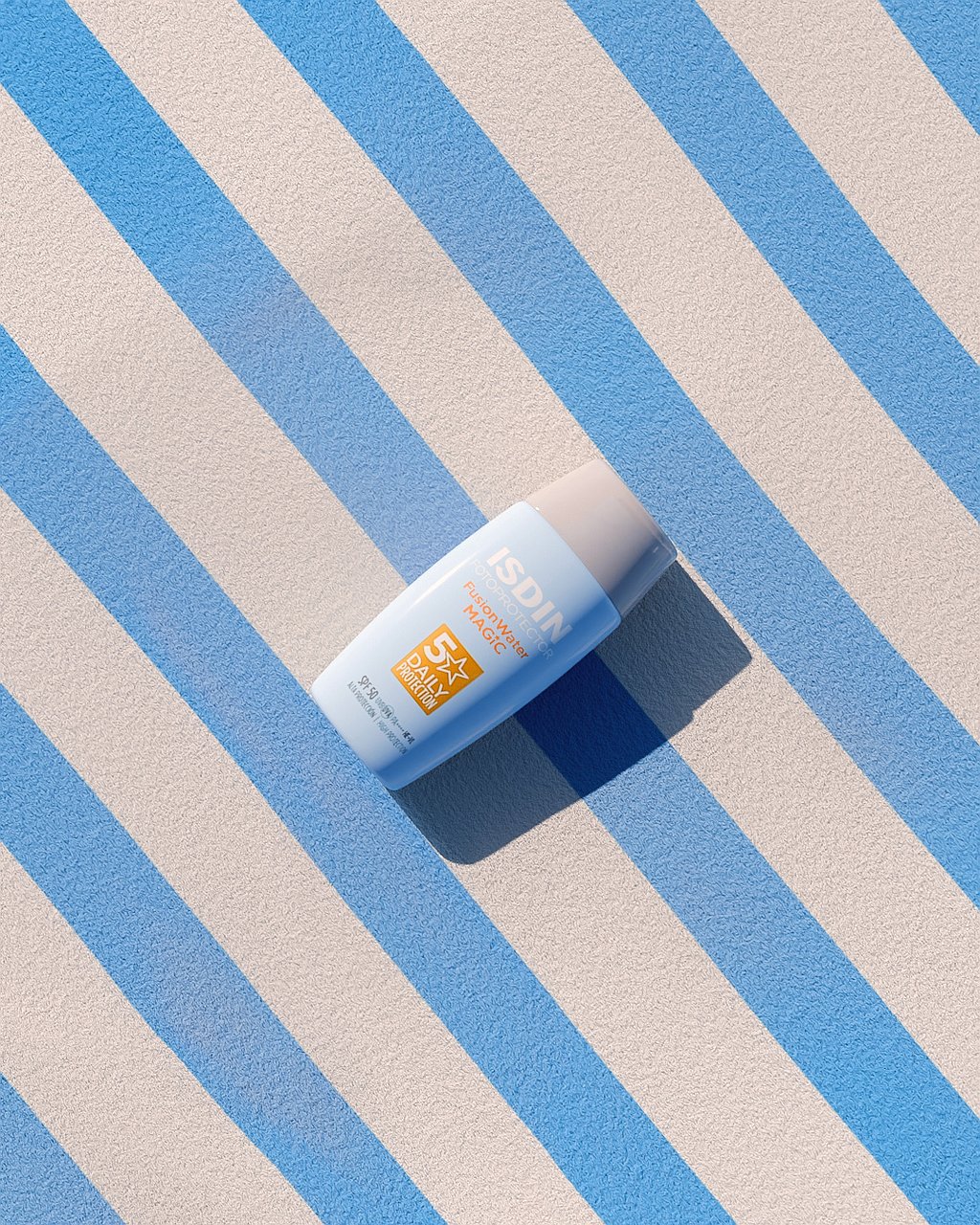 Bote de crema de sol de la marca ISDIN encima de una toalla, de color blanca y azul.