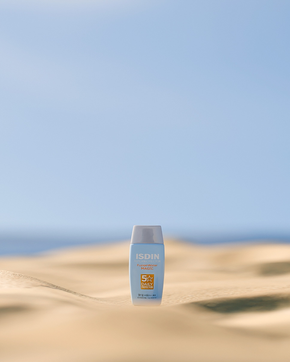 Bote de crema solar de la marca ISDIN en la playa.