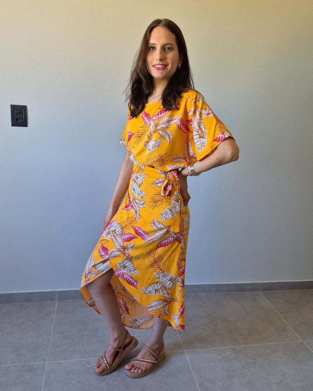 Mulher em pé usando uma saia envelope amarela, com estampa de folhas.
