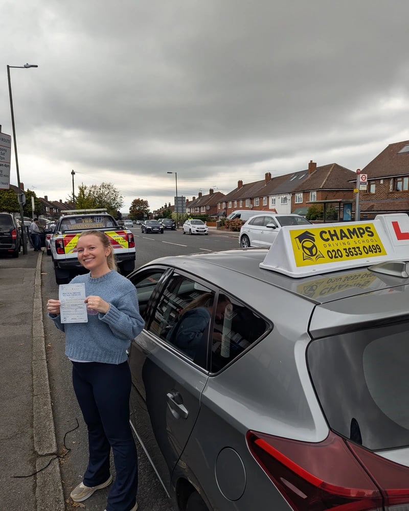 A happy student holding her practical driving test pass certificate next to a Champs Driving School car.