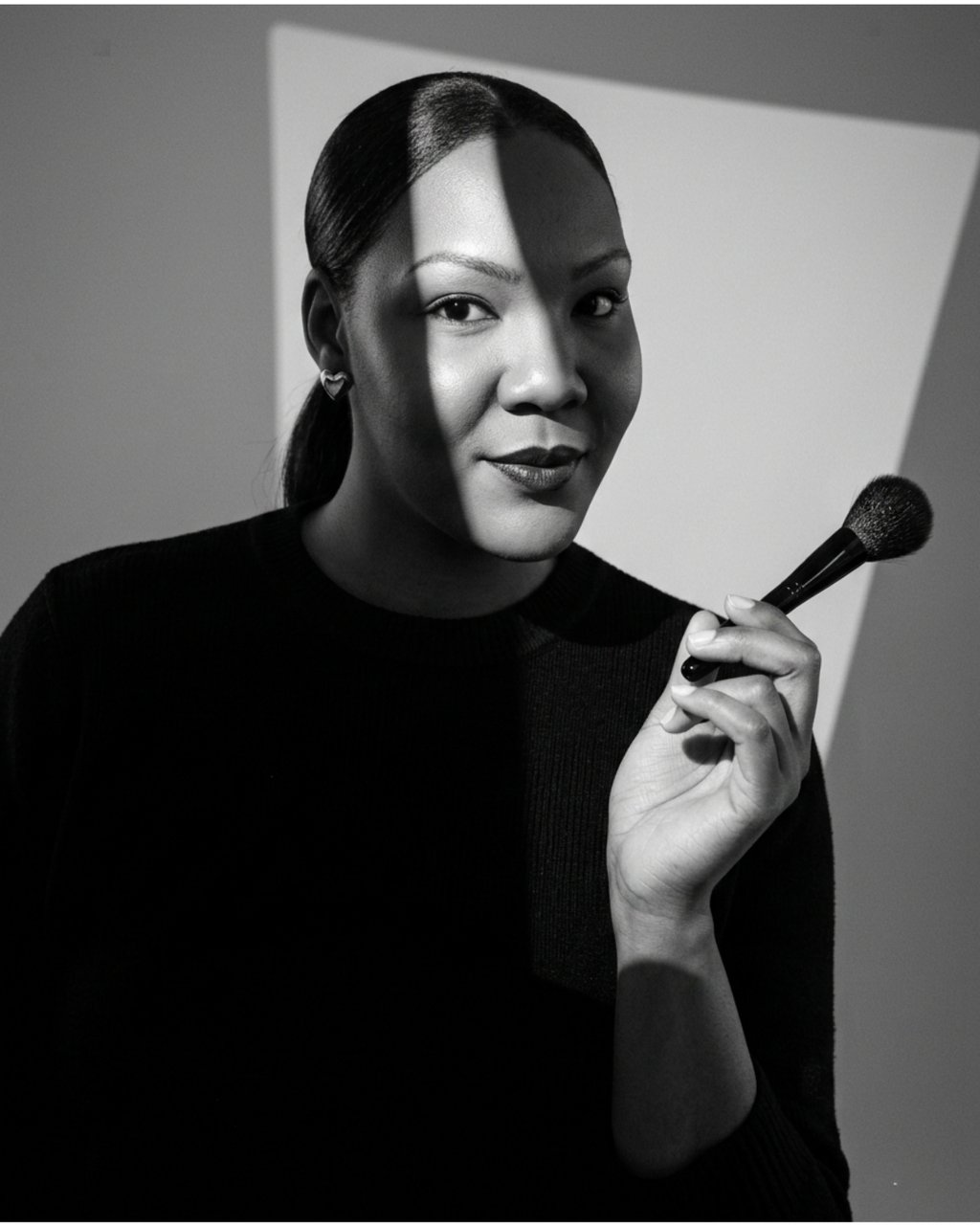 Black and white portrait of a makeup artist holding a professional cosmetic brush with artistic shadows.