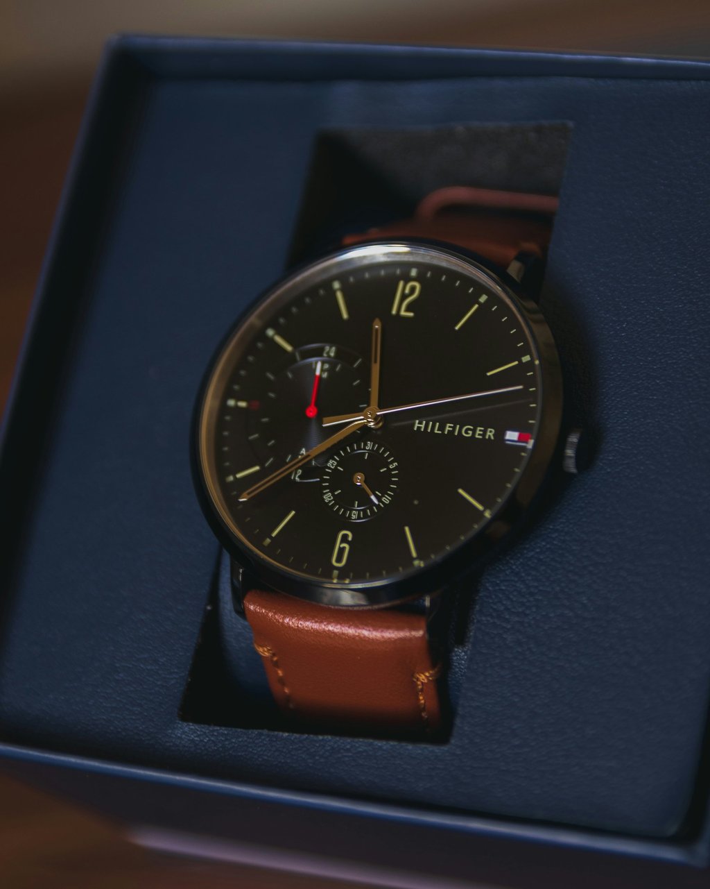 A luxury Tommy Hilfiger men's analog watch with a black dial and brown leather strap in a gift box.