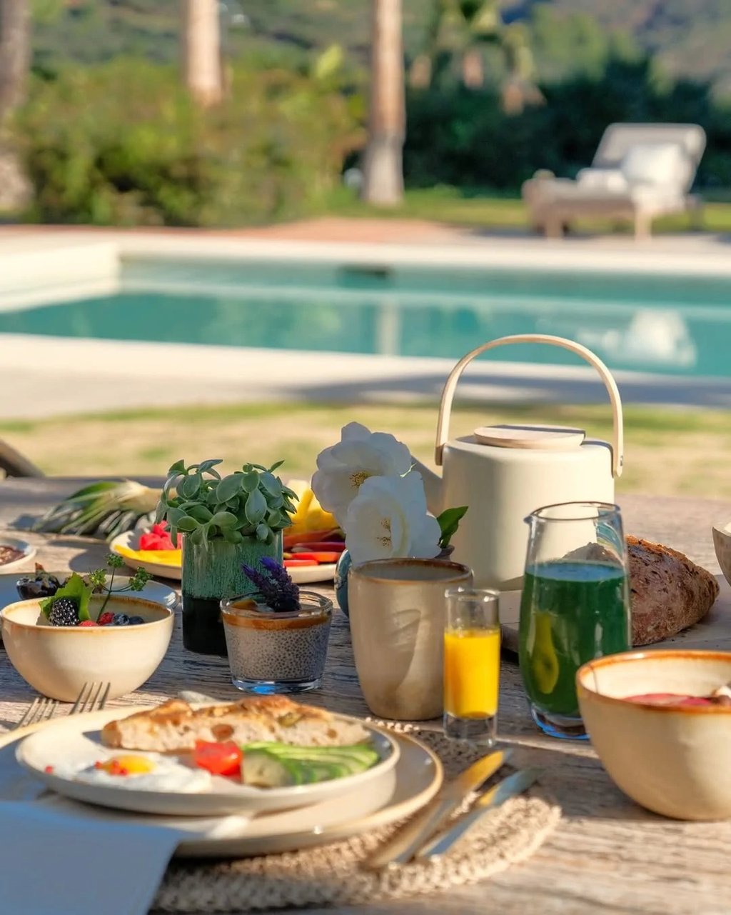 Poolside breakfast setup with juice, bread and garden views