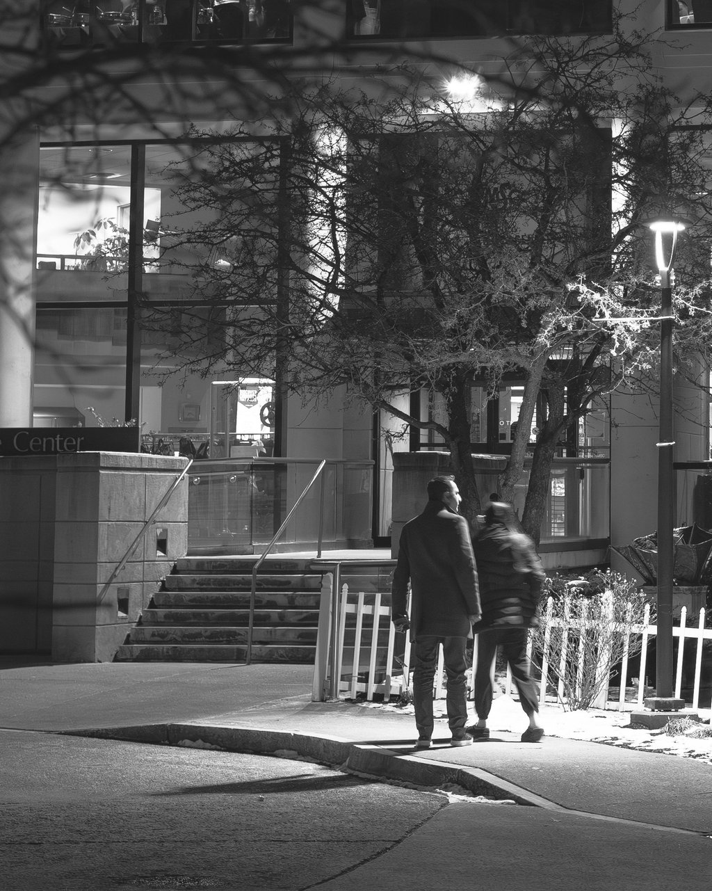 Black and White Photo of a couple walking at night below the glow of a street lamp.